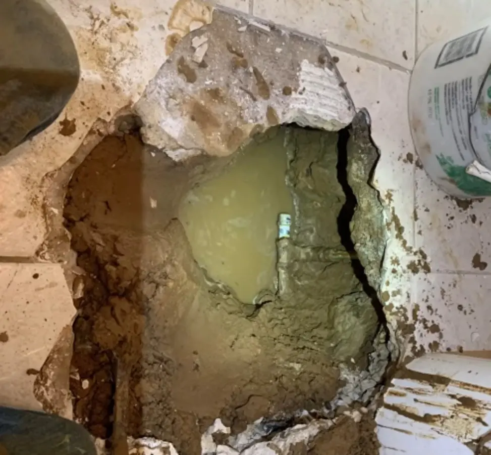 A concrete slab opened at a confirmed leak, with water pooled around a pipe in the soil below